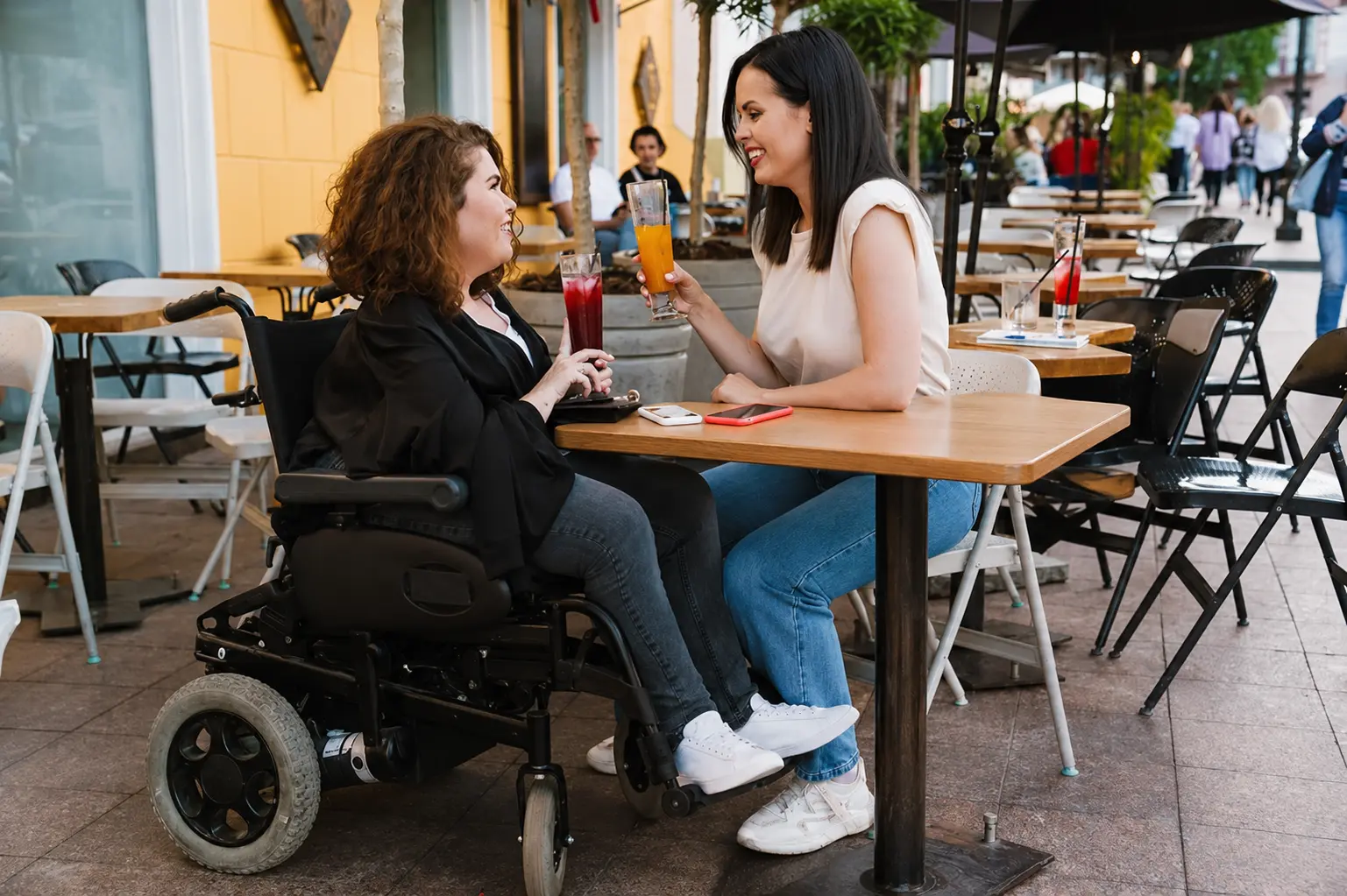 Two women sharing a drink and talking at an accessible cafe table